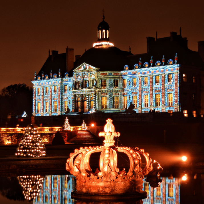 Vaux-le-Vicomte Christmas Castle Lights Illuminated Château de Vaux-le-Vicomte at night with a glowing crown sculpture and Christmas trees reflected in the water