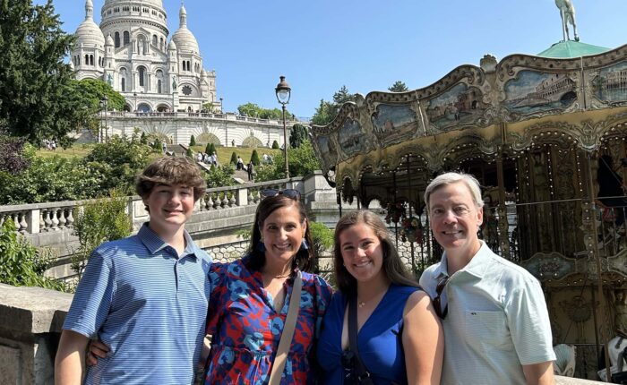 Family of four smiling by the Montmartre carousel with Sacré-Cœur basilica rising above them on a sunny private tour.