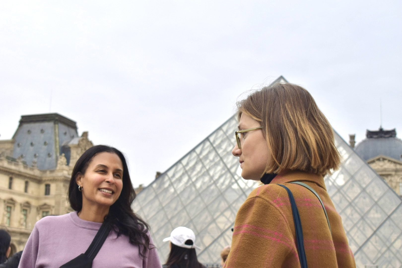 Two women chat with their guide outside the Louvre, with the glass pyramid rising behind them