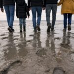 Group walking tidal flats footprints reflections toward Mont Saint-Michel low tide - Paris and Beyond Tours from Bayeux Caen