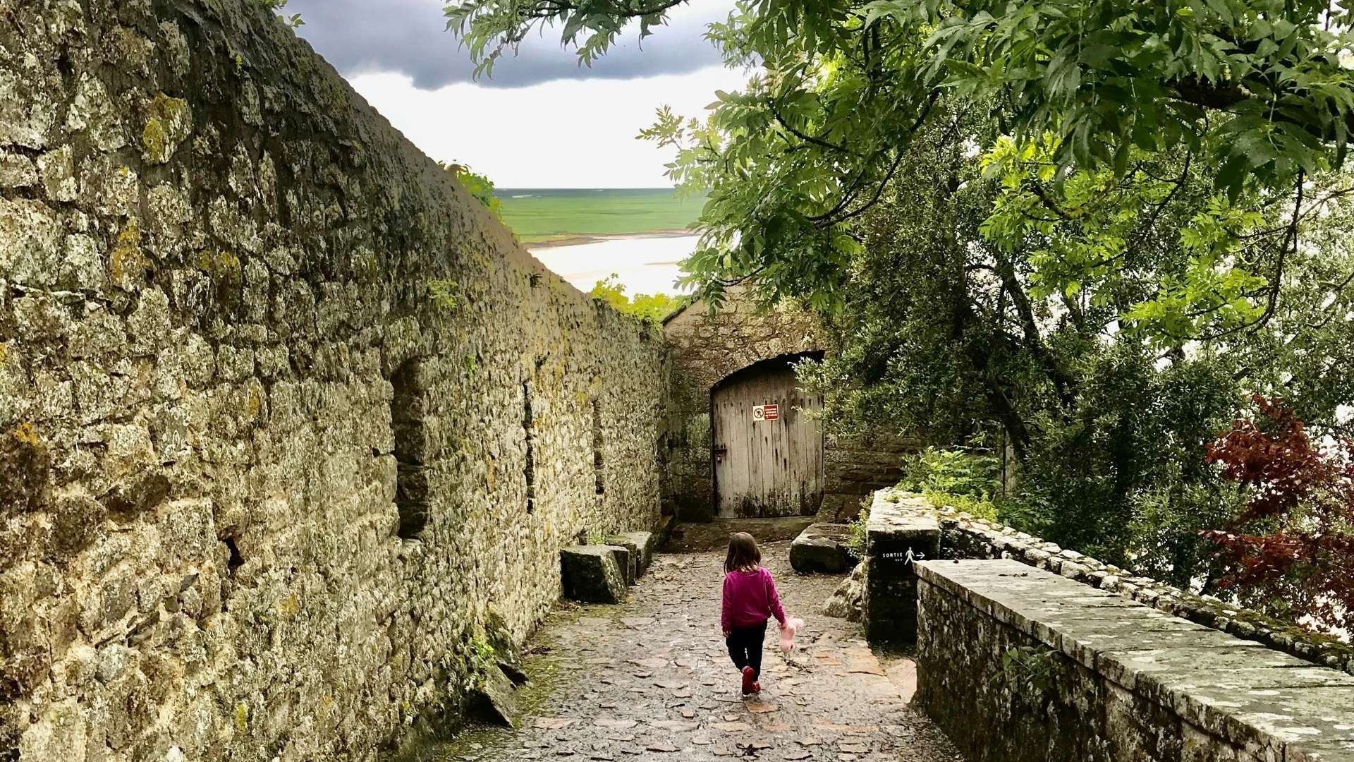 Mont Saint-Michel Medieval Village Walk Paris and Beyond Tours Family Normandy Tour Paris and Beyond Tours child exploring Mont Saint-Michel medieval cobblestone rampart path with ancient stone walls and tidal bay view family Normandy tour from Bayeux Caen