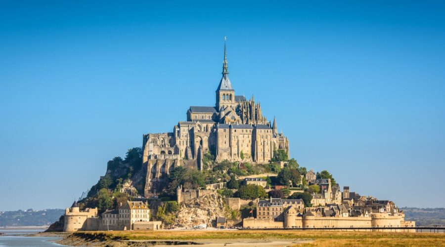Mont Saint-Michel abbey fortress rising from tidal bay with medieval village and fortifications during low tide - Paris and Beyond Tours private Normandy day trip from Bayeux Caen