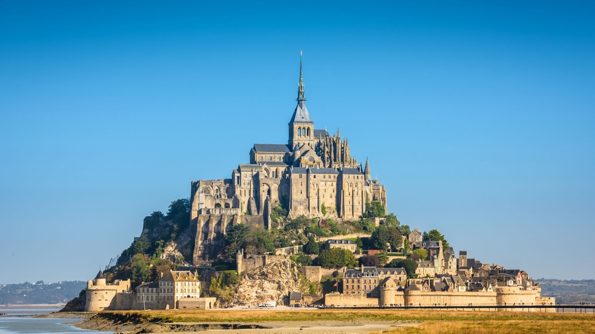 Mont Saint-Michel Classic Island View | Paris and Beyond Tours Normandy from Bayeux Caen Mont Saint-Michel abbey fortress rising from tidal bay with medieval village and fortifications during low tide - Paris and Beyond Tours private Normandy day trip from Bayeux Caen